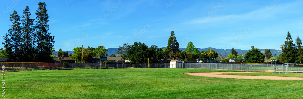 Panoramic view of an empty softball, baseball field, trees and green grass in typical american residential suburban neighborhood