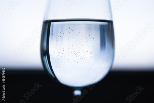Transparent wine glass with water in the middle. Blue black white blurred background. Small bubbles