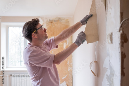 Obraz na płótnie Caucasian man tearing off old wallpaper from wall preparing for home redecoratio