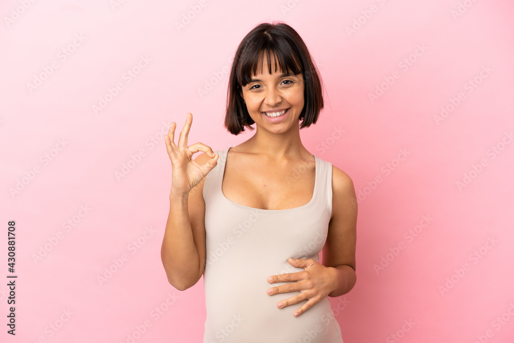 Young pregnant woman over isolated pink background showing ok sign with fingers