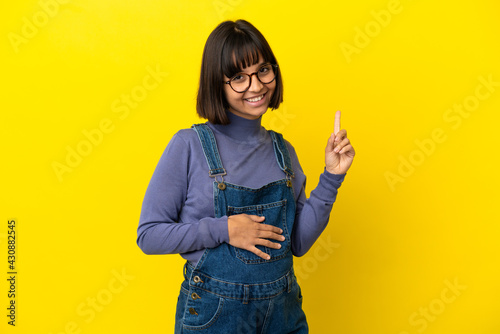 Young pregnant woman over isolated yellow background pointing up a great idea