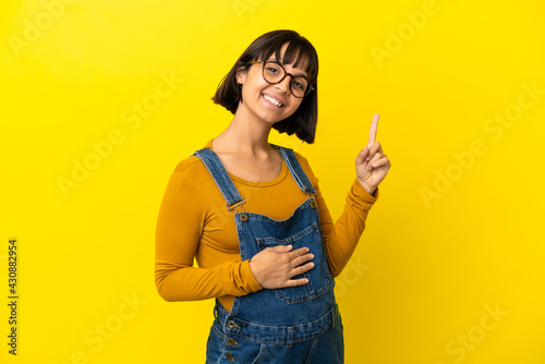 Young pregnant woman over isolated yellow background showing and lifting a finger in sign of the best