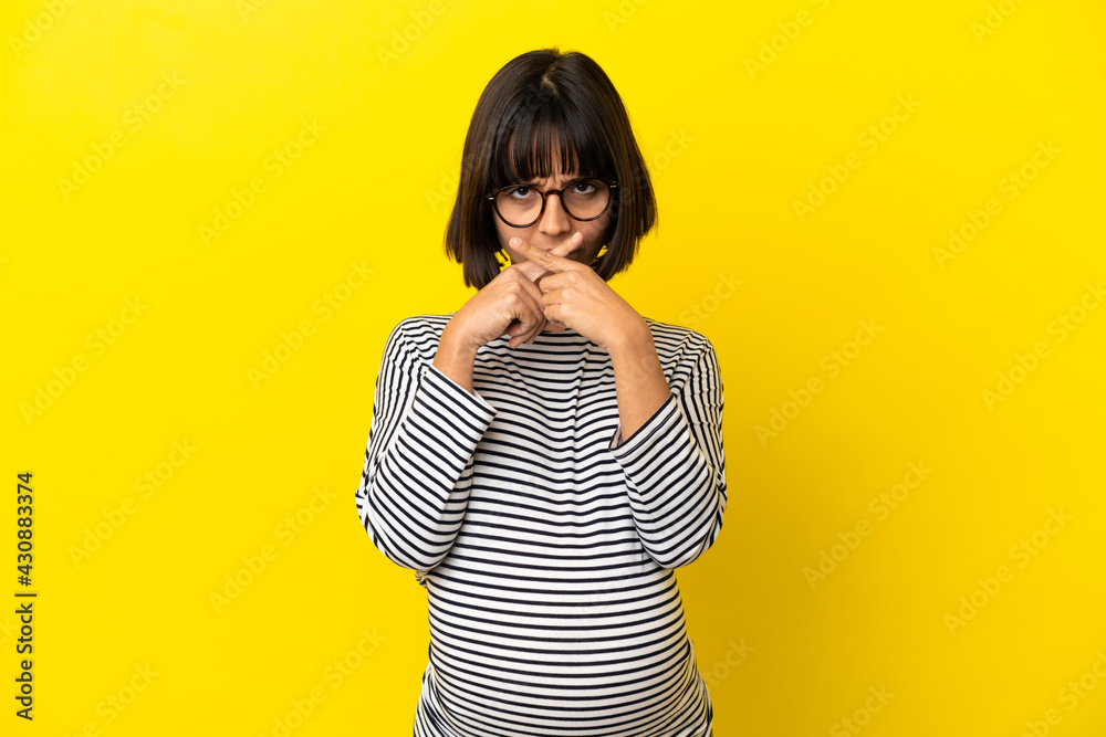 Young pregnant woman over isolated yellow background showing a sign of silence gesture Young pregnant woman over isolated yellow background showing a sign of silence gesture