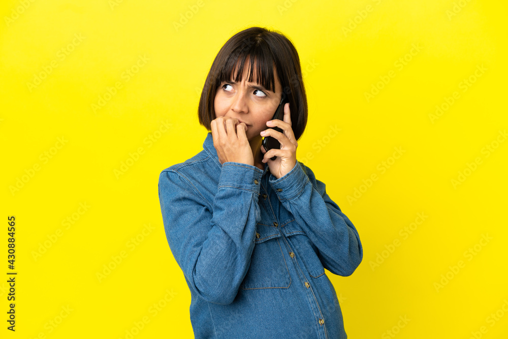 Pregnant woman using mobile phone isolated on yellow background having doubts Pregnant woman using mobile phone isolated on yellow background having doubts
