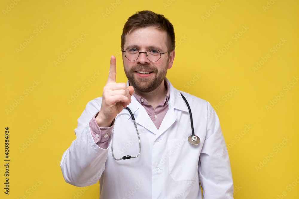 Calm, benevolent doctor raised his index finger up, he found a solution to the problem and is very happy. Yellow background. Calm, benevolent doctor raised his index finger up, he found a solution to the problem and is very happy. Yellow background.