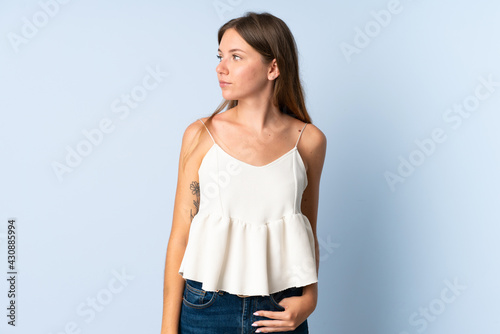 Young Lithuanian woman isolated on blue background having doubts while looking side