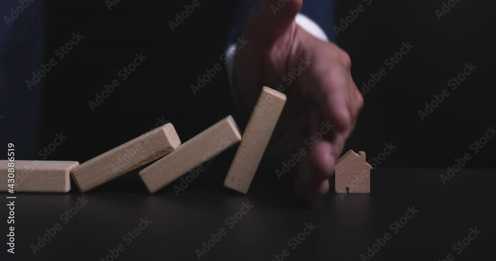 4K Video slow close up hand stop domino effect to make house icon fall . business concept of try to stop the domino effect in real estate industry.