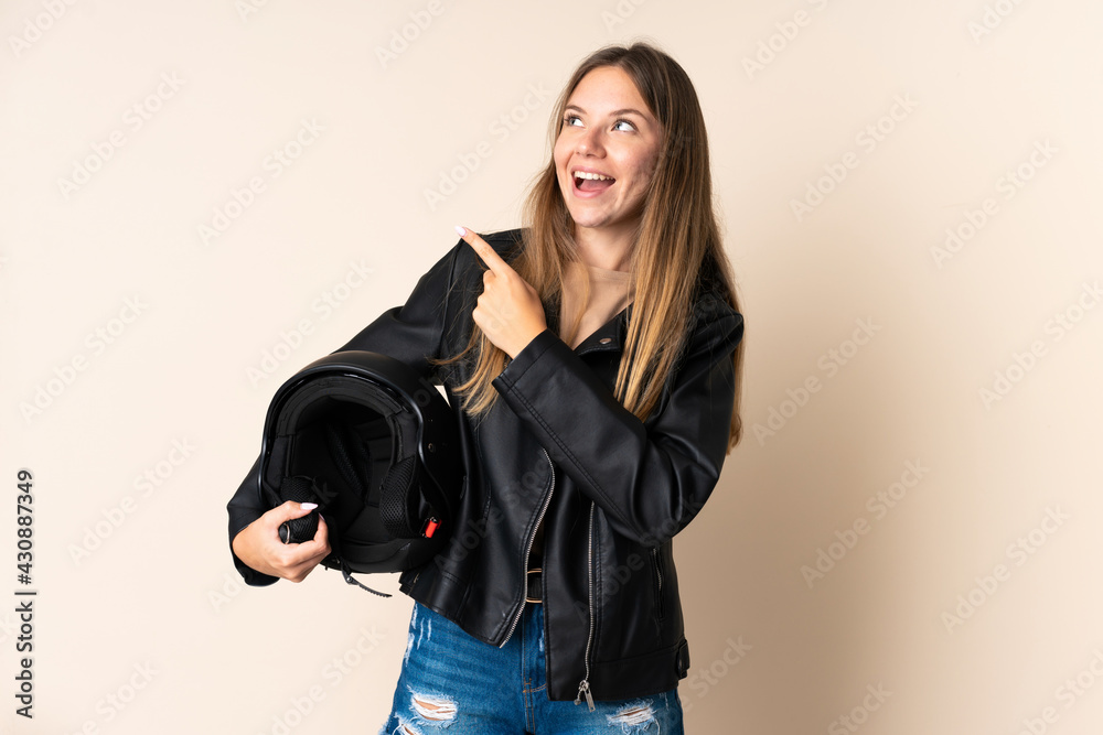 Young Lithuanian woman holding a motorcycle helmet isolated on beige background intending to realizes the solution while lifting a finger up Young Lithuanian woman holding a motorcycle helmet isolated on beige background intending to realizes the solution while lifting a finger up