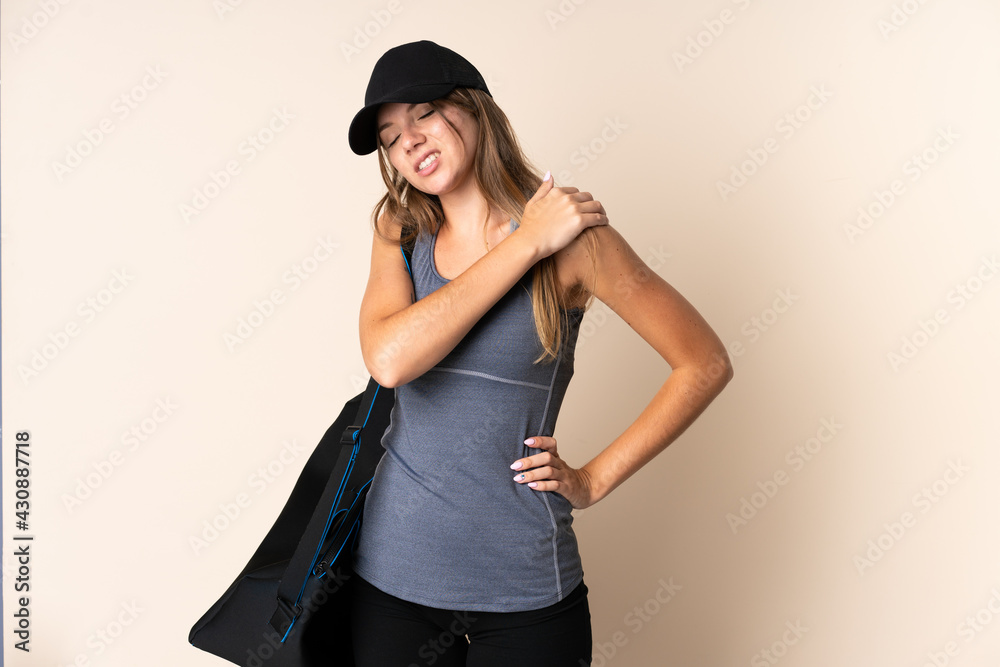 Young sport Lithuanian woman holding a sport bag isolated on beige background suffering from pain in shoulder for having made an effort Young sport Lithuanian woman holding a sport bag isolated on beige background suffering from pain in shoulder for having made an effort