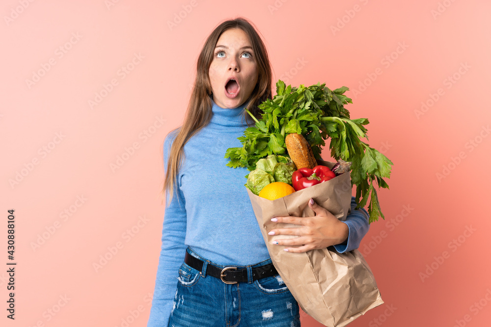 Young Lithuanian woman holding a grocery shopping bag looking up and with surprised expression Young Lithuanian woman holding a grocery shopping bag looking up and with surprised expression