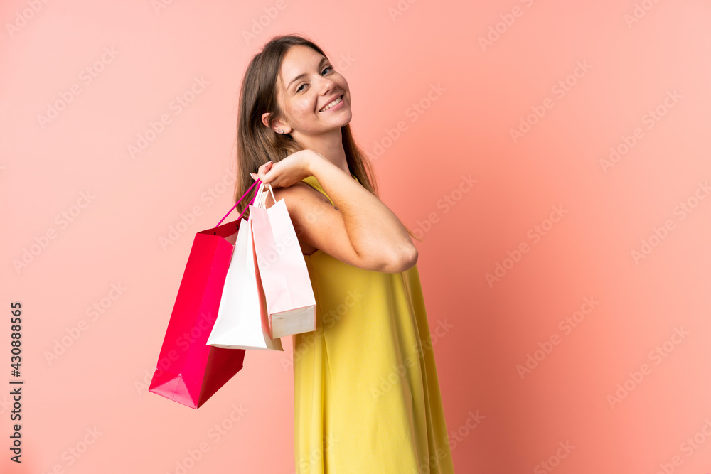 Young Lithuanian woman isolated on pink background holding shopping bags and smiling