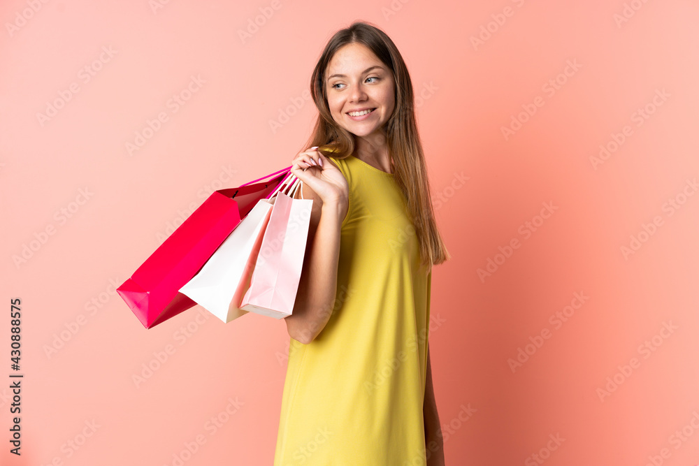 Young Lithuanian woman isolated on pink background holding shopping bags and looking back