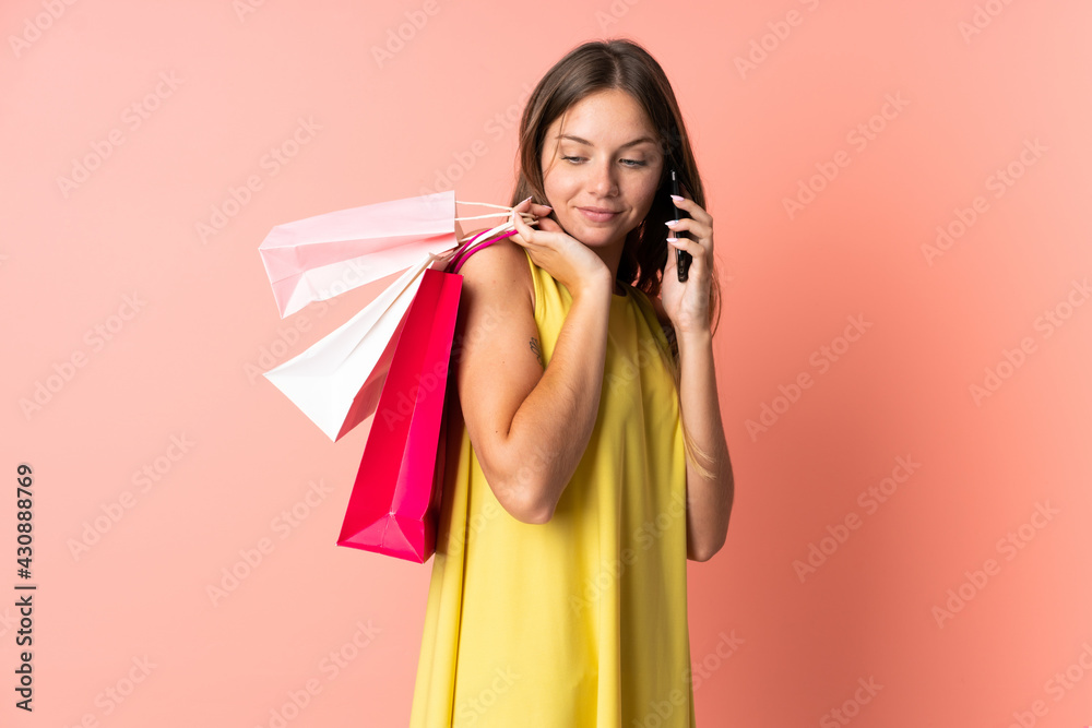 Young Lithuanian woman isolated on pink background holding shopping bags and calling a friend with her cell phone Young Lithuanian woman isolated on pink background holding shopping bags and calling a friend with her cell phone