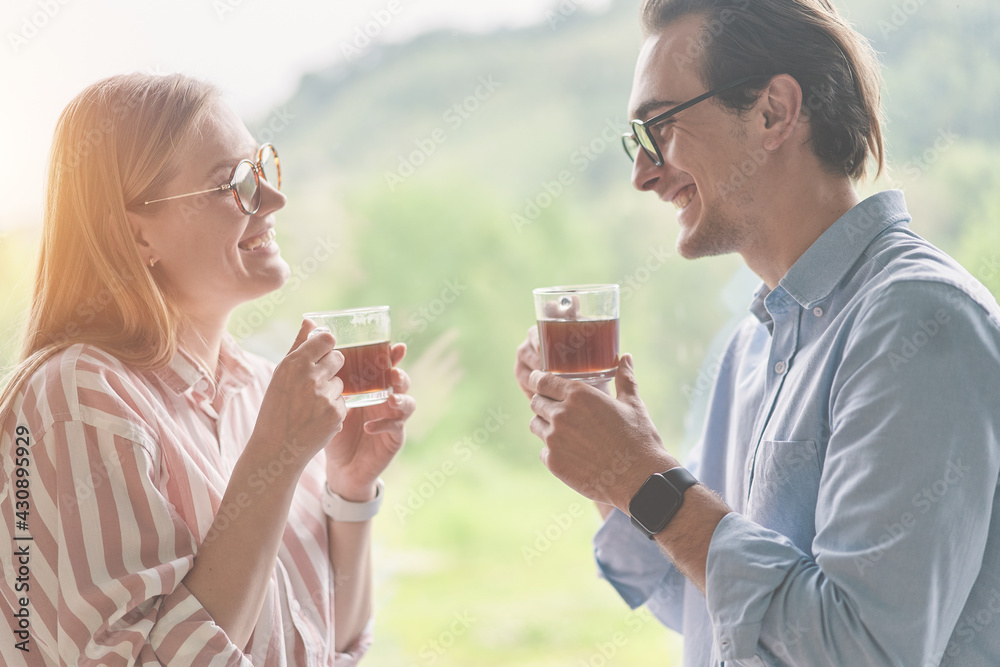 Side view of successful happy couple with glasses drinking morning coffee near the window