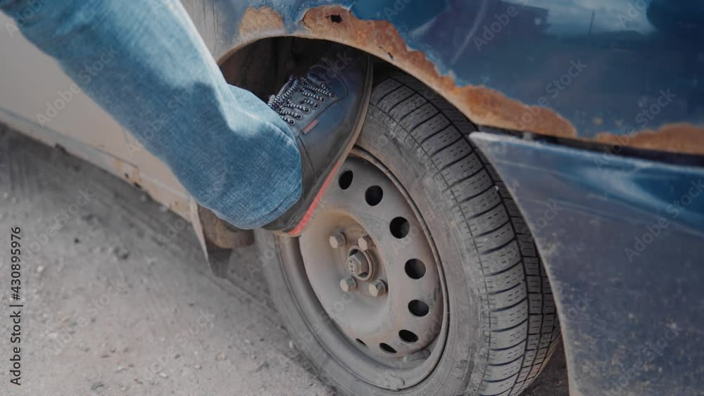 the man rests his foot on the wheel of the car and presses it to check ...