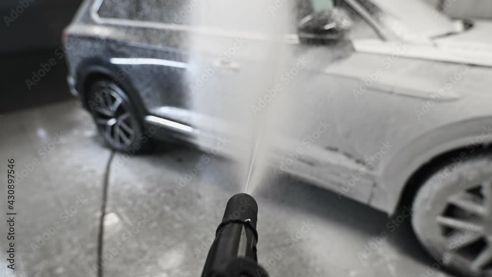 Man covering a car with foam using high pressure washer. Car washing process. First-person view.