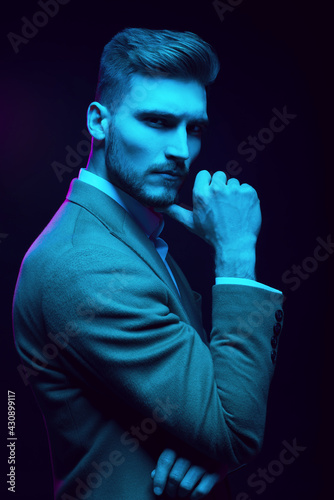Young handsome model posing in a studio in a trendy neon light. Fashionable man in a stylish suit. Vibrant color. Bright colorful light effects. Disco style. Overlay. Gel filter. Supersaturated