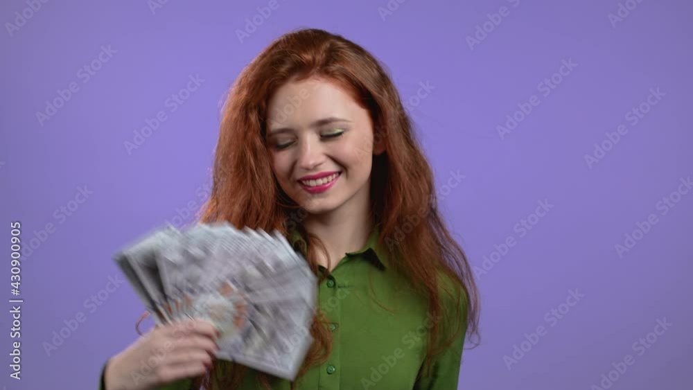 Smiling happy woman with cash money - USD currency dollars banknotes on violet wall. Symbol of jackpot, gain, victory, winning the lottery Smiling happy woman with cash money - USD currency dollars banknotes on violet wall. Symbol of jackpot, gain, victory, winning the lottery