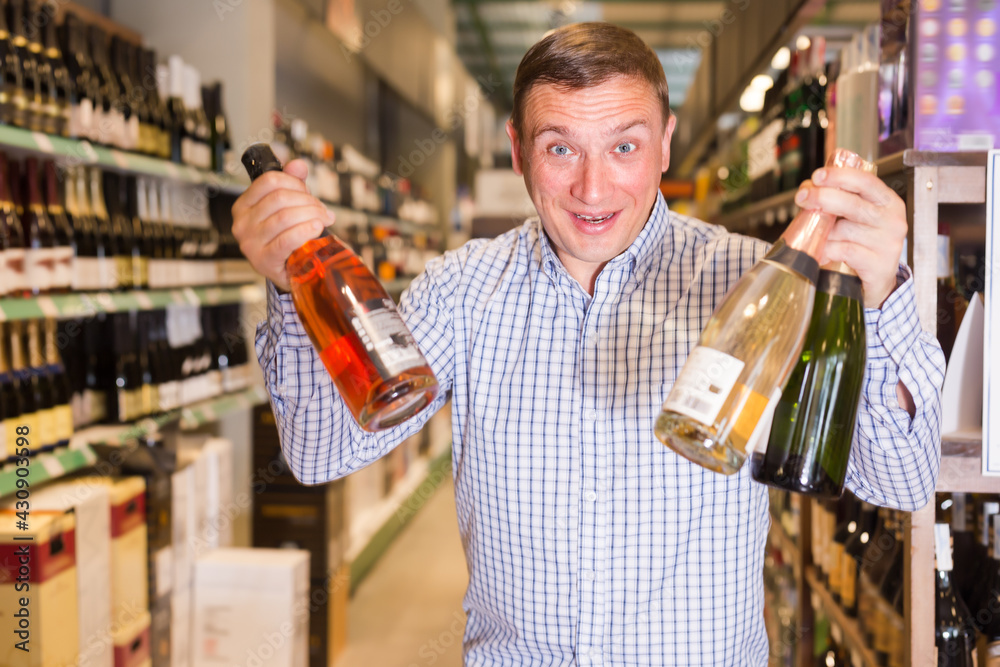 Portrait of positive man buying wine in supermarket