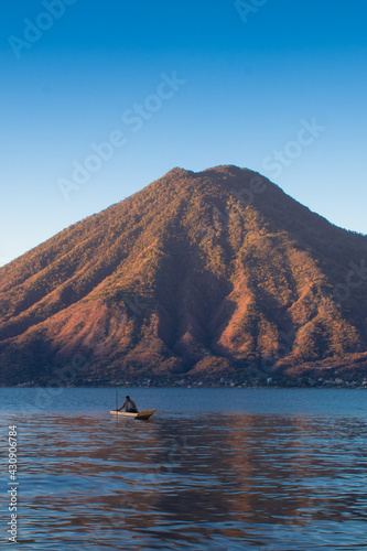 man sailing in a wooden boat on a lake in the middle of a beautiful sunrise with a dormant volcano in the background