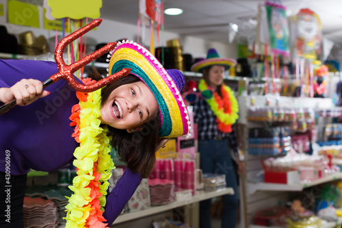 Portrait of positive comically dressed girl joking in festive accessories shop