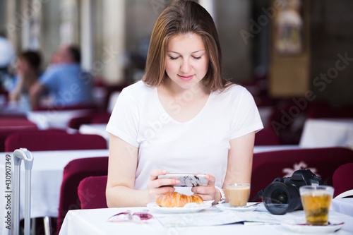Smiling woman tourist using mobile phone in cafe