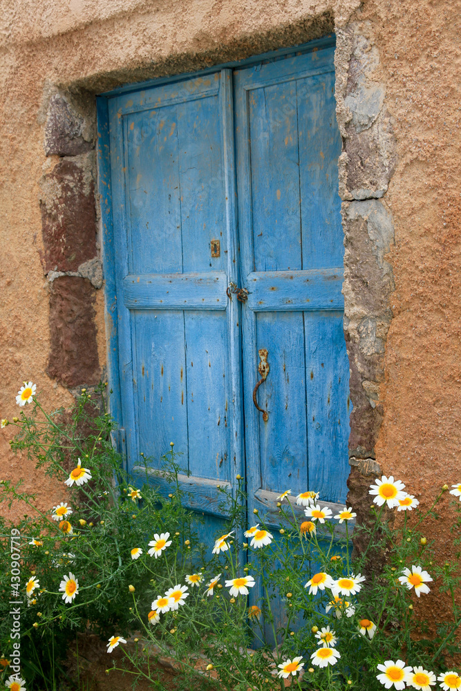 Painted blue wood window in stone wall with yellow flowers, Mykonos, Greece Painted blue wood window in stone wall with yellow flowers, Mykonos, Greece
