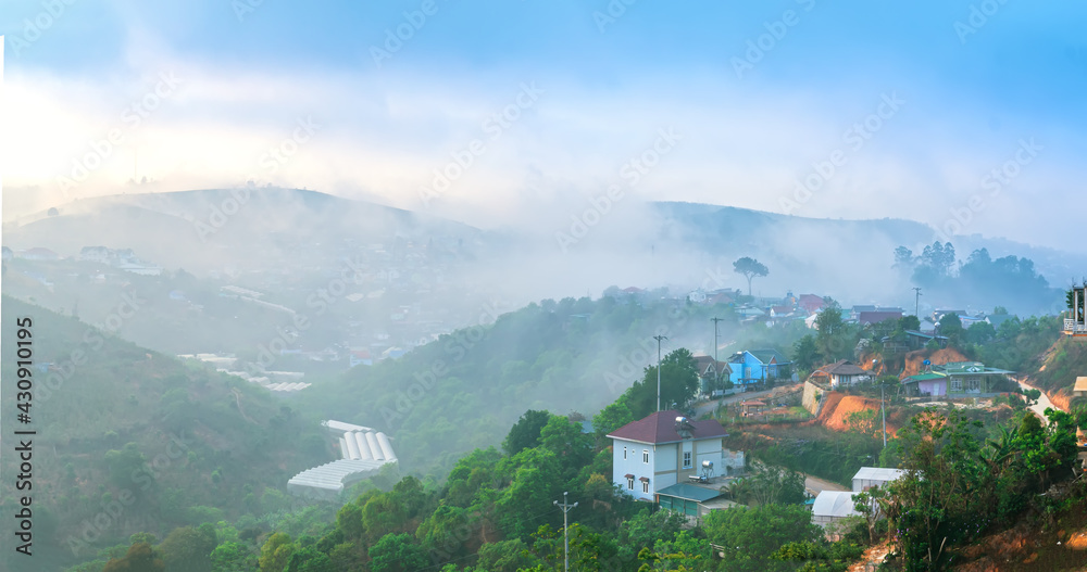 Fototapeta premium A small town under a tea hill valley in the morning with mist covering in the highlands of Da Lat, Vietnam. The place provides a great deal of tea for the whole country