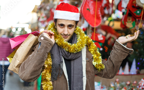 Smiling man in Christmas hat with purchases delighted at Christmas fair