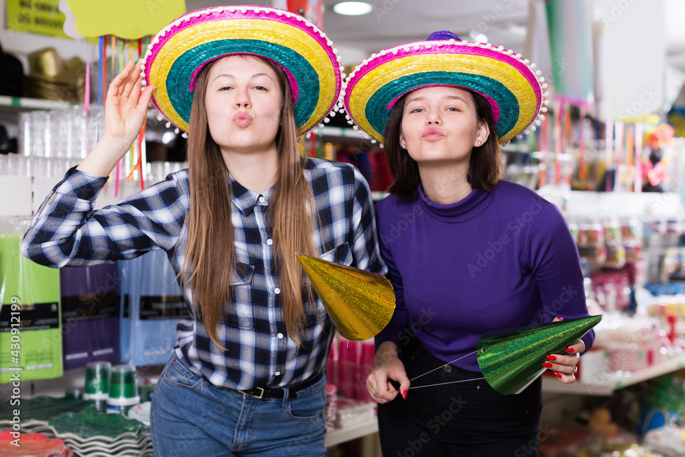 Positive young girls enjoying on party hats in festive accessories shop