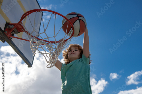 Basketball kids game. Cute little child boy holding a basket ball trying make a score, outdoor on playground.