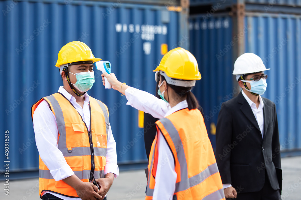 female Asian worker measures temperature with a thermometer for employees before entering a container yard. People working on the import and export concept. Professional engineering team. female Asian worker measures temperature with a thermometer for employees before entering a container yard. People working on the import and export concept. Professional engineering team.