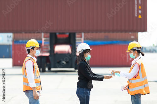 female Asian worker measures temperature with a thermometer for employees before entering a container yard. People working on the import and export concept. Professional engineering team.