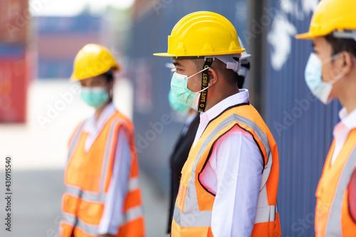 Group of professional team worker wearing protection face mask during coronavirus and flu outbreak and wearing safety hardhat helmet at container yard or cargo warehouse
