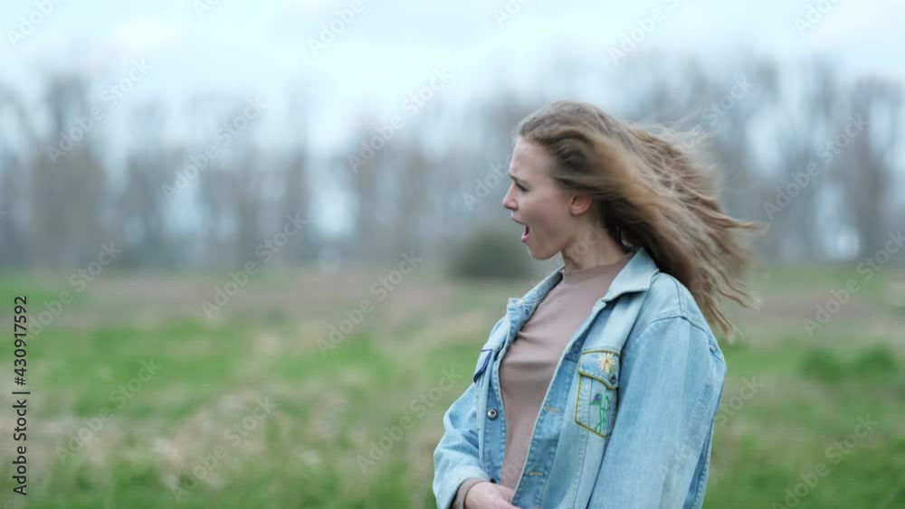 [4k] surprised blonde woman in heavy wind on meadow