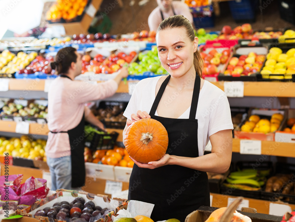 Young woman with pumpkin in hands and man on background in greengrocery
