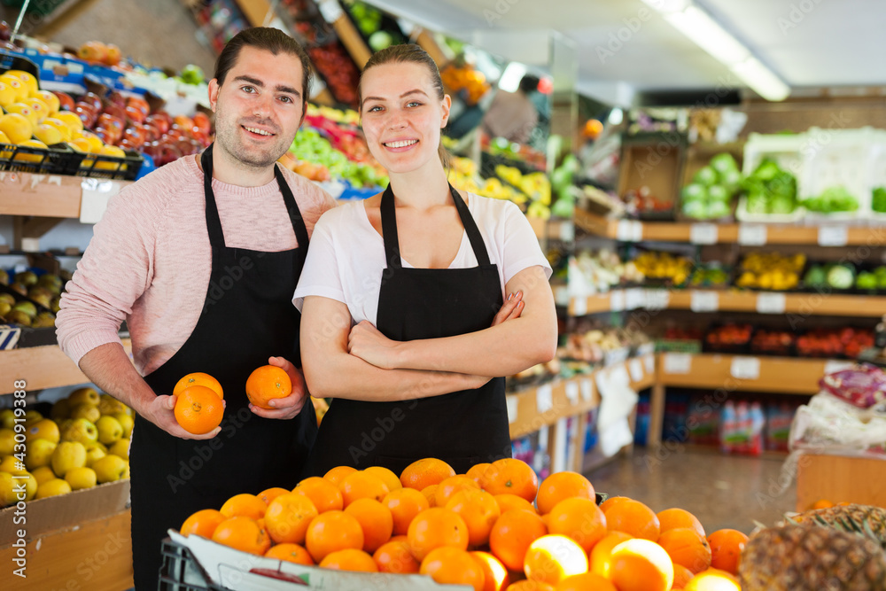Young man and woman wearing aprons holding fresh oranges on the supermarket