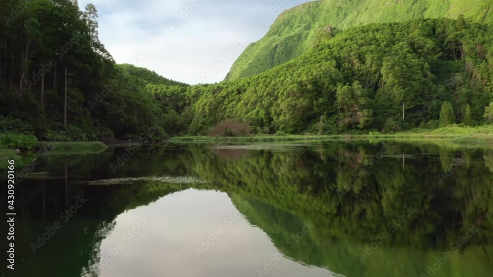 Drone flying over water surface of the lake in Poco Ribeira do Ferreiro, Alagoinha, Flores Island, Azores, Portugal, Europe. Green landscape with forest and mountains, 4k footage
