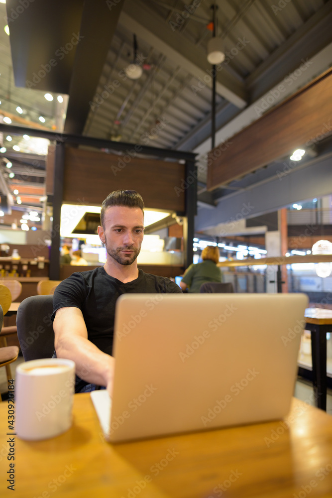 Portrait of handsome man sitting at coffee shop using laptop computer Portrait of handsome man sitting at coffee shop using laptop computer