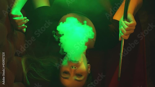 A girl smokes a hookah in a nightclub with a green light. Top view photo
