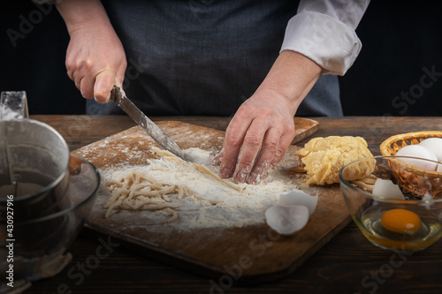 Women's hands, flour and dough. A woman in an apron cooking dough for homemade baking, a rustic home cozy atmosphere, a dark background with unusual lighting.