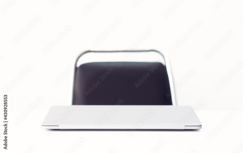 A gray notebook is placed on a white desk, taken from the front corner, behind a black chair. The white background has a copy space concept on the workplace, conference table, director's desk. A gray notebook is placed on a white desk, taken from the front corner, behind a black chair. The white background has a copy space concept on the workplace, conference table, director's desk.