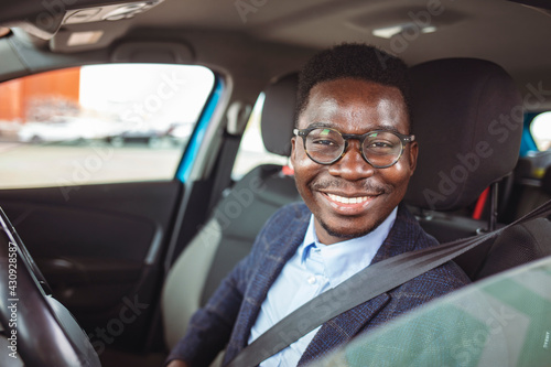 Young happy man fastening his seatbelt before a trip by car and looking at camera. Portrait of young hispanic man sitting in driving seat of car, fastening safety belt and making en eye contact © Dragana Gordic