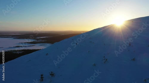 Aerial view of a person snowshoeing up on a snowy mountain, sunrise, in Lapland - tracking, drone shot photo