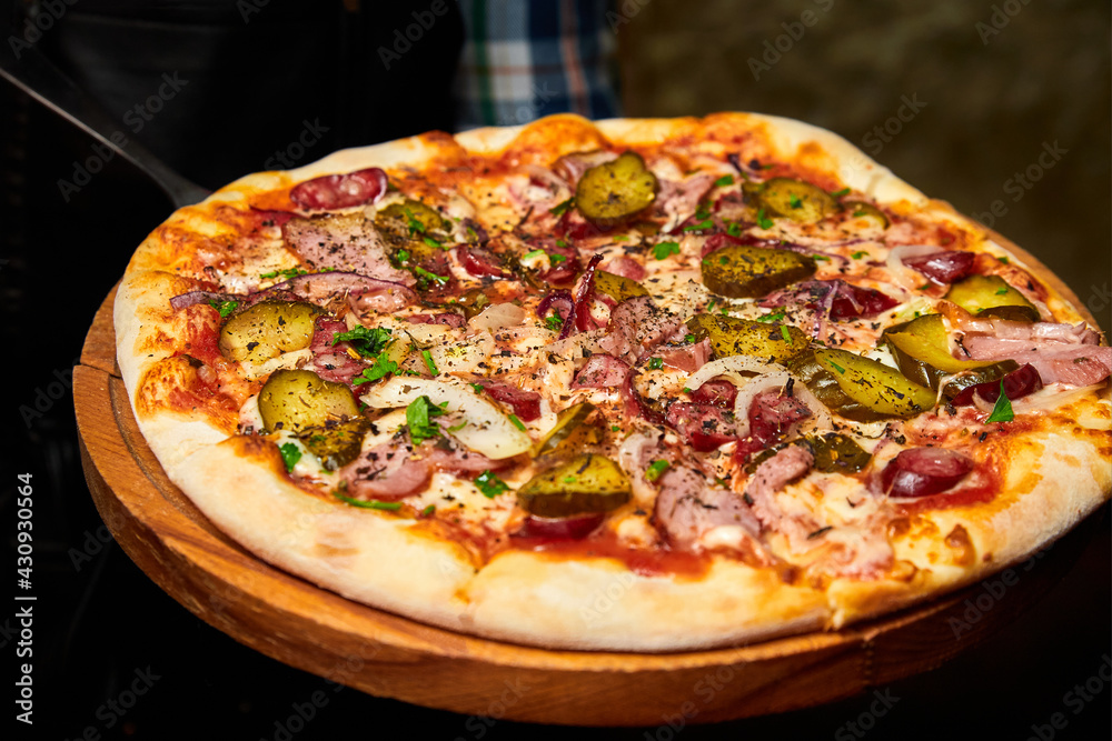 Waiter holds a Fresh pizza pickles, bacon, sausages and cheese on a wooden board. Close-up, selective focus