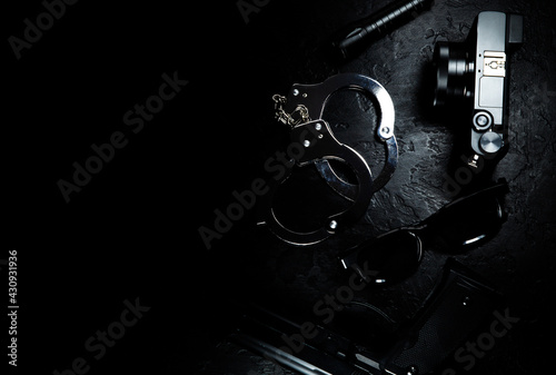 Black gun, flashlight, glasses, camera and Police metal real handcuffs lie on the black background. Private detective work. Searching information. Crime and robbery, prison concept.