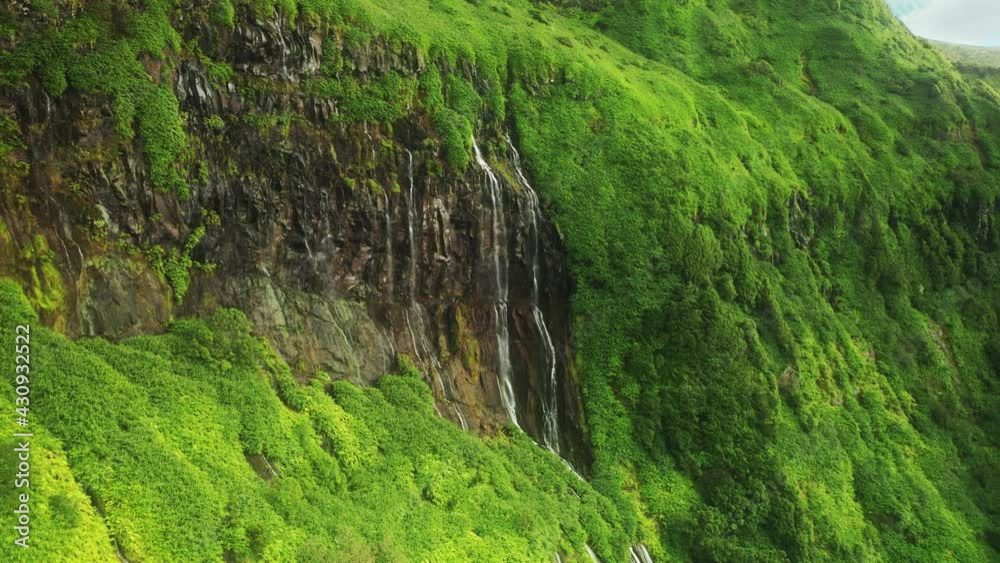 Drone shot of picturesque cascading waterfalls of Poco Ribeira do Ferreiro, Alagoinha, Flores Island, Azores, Portugal, Europe. Scenic view of mountains covered green vegetation, 4k footage