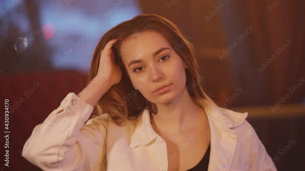 Portrait of a young beautiful girl in a nightclub. The girl straightens her hair and looks at the camera Portrait of a young beautiful girl in a nightclub. The girl straightens her hair and looks at the camera