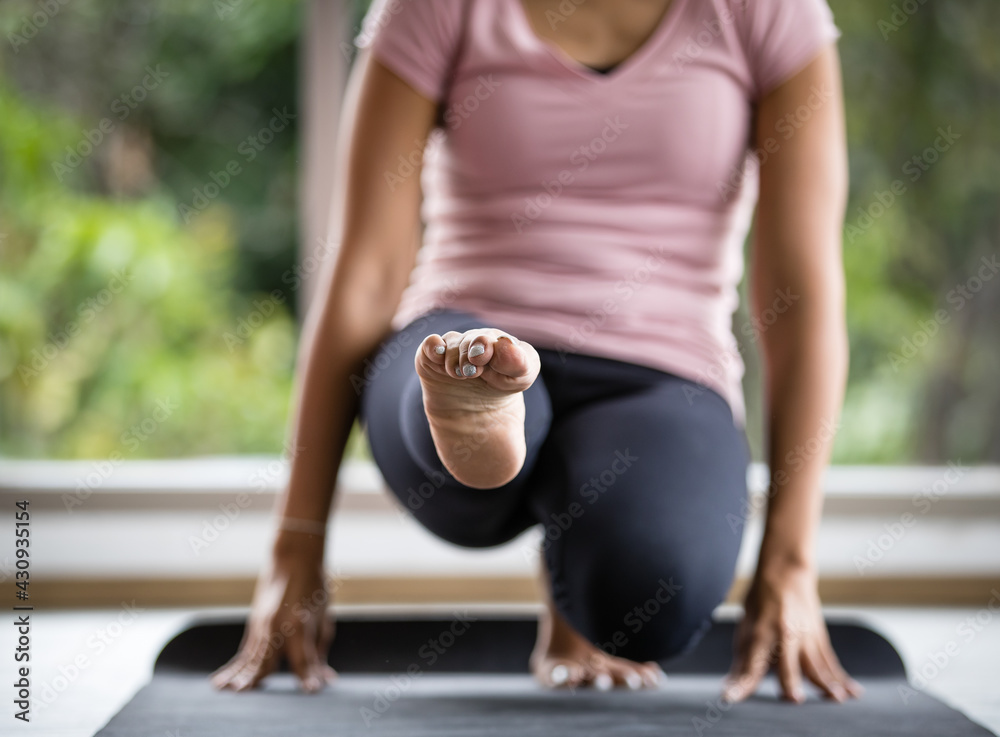Selective focus and close up to female body wearing pink sport shirt and black elastic pants, doing exercise in indoor gym or home, practicing yoga, putting hand on floor and lifting herself up.
