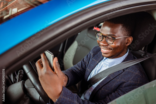 Man looking at mobile phone while driving. Portrait of a man using his cell phone while driving. Young man using his smartphone behind the wheel.